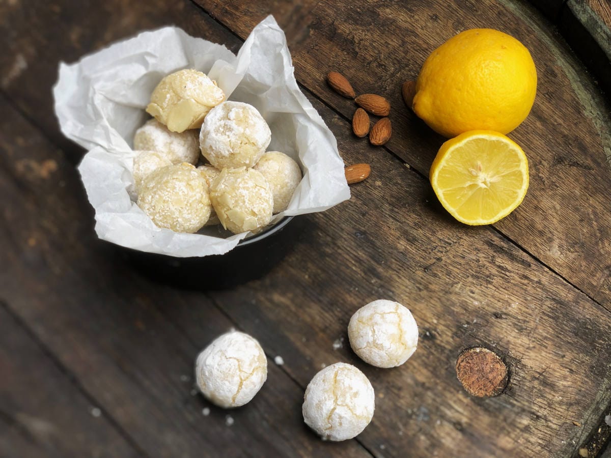 Hausgemachte Zitronen-Mandel-Plätzchen (Amaretti) in einer Schale auf rustikalem Holztisch, dekoriert mit Mandeln und frischen Zitronen.