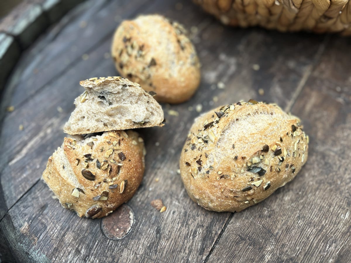 Selbst gebackene Körnerbrötchen mit verschiedenen Saaten, frisch aufgeschnitten auf rustikalem Holztisch.