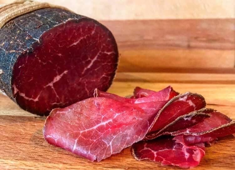 Dunkelrotes, fein aufgeschnittenes, geräuchertes Rindfleisch auf einem Holzbrett, traditionell gereift und serviert.